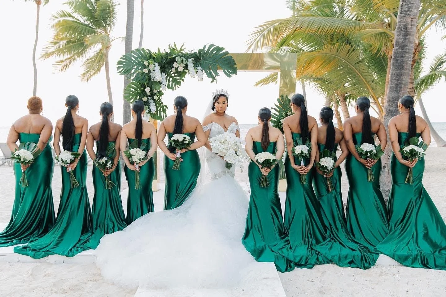 Bridesmaids in emerald green gowns, backs turned at a beach wedding